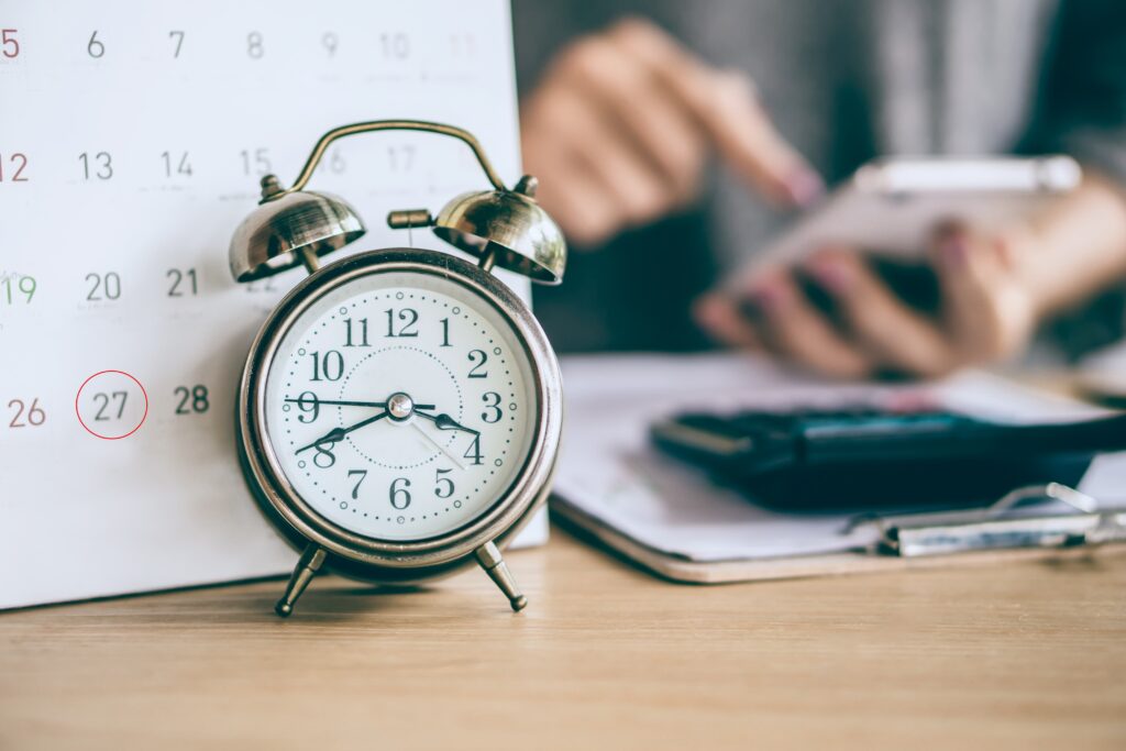 A lawyer sitting at a desk with an alarm clock, using her phone setting timeline for criminal defense case