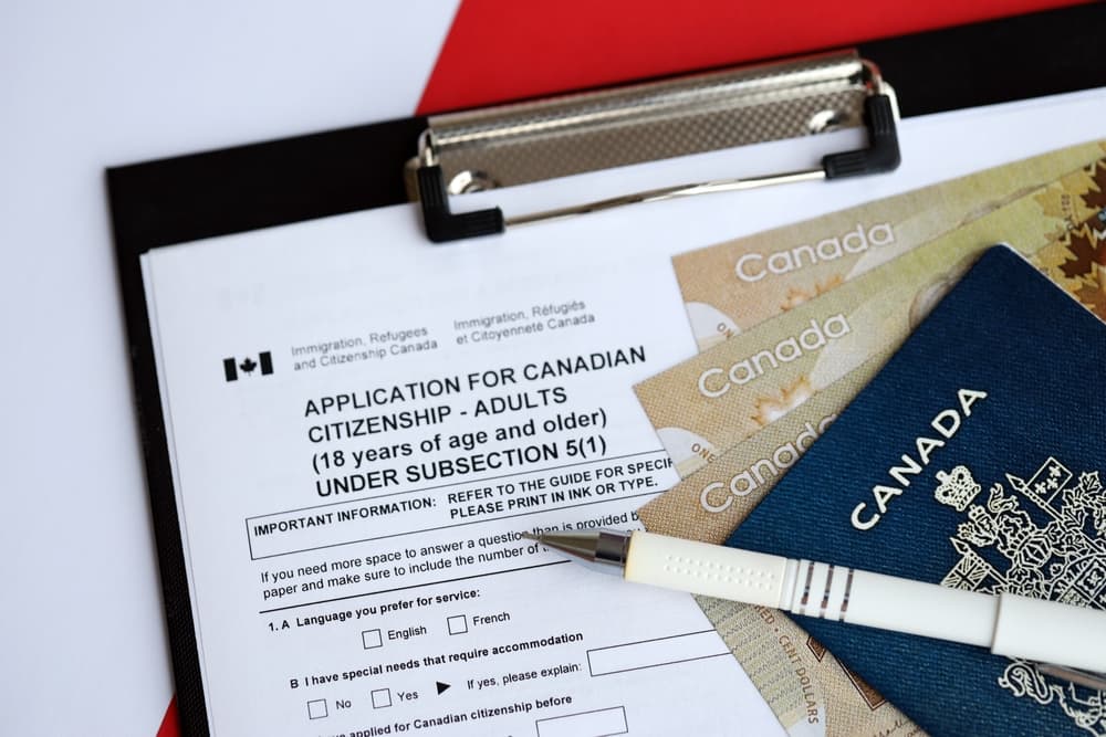 An Application for Canadian citizenship for adults on a table, with a pen, passport, and dollar bills nearby, close up.