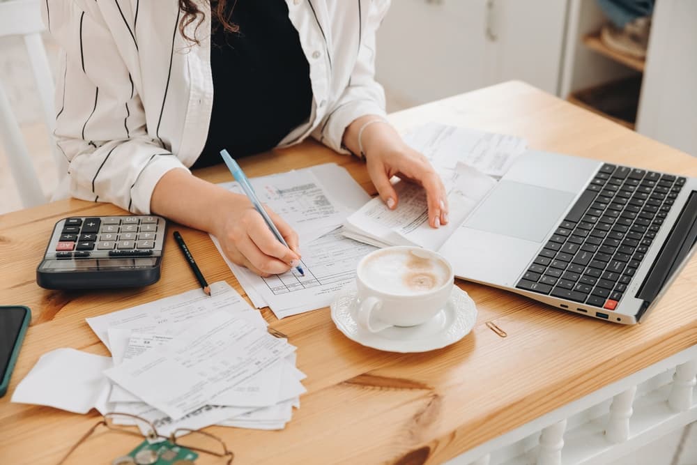 Close-up of an unrecognizable woman's hands working at home in the kitchen, sorting financial papers, using a calculator, paying bills, and planning a budget.