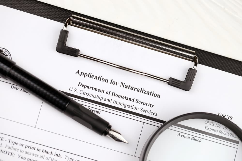 A blank N-400 Application for Naturalization form on an A4 tablet lies on an office table, accompanied by a pen and a magnifying glass, close up.