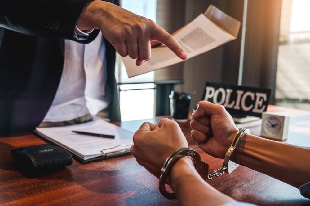 A police officer interrogates a handcuffed male suspect in an investigation room after a crime.