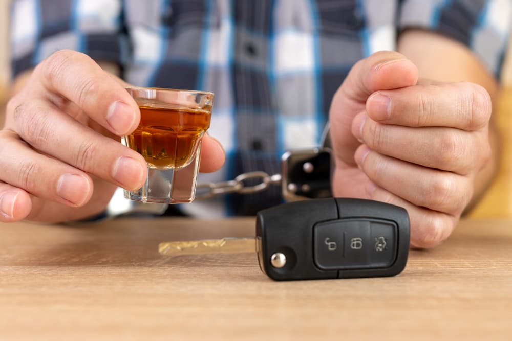 A glass of alcohol next to a set of car keys.