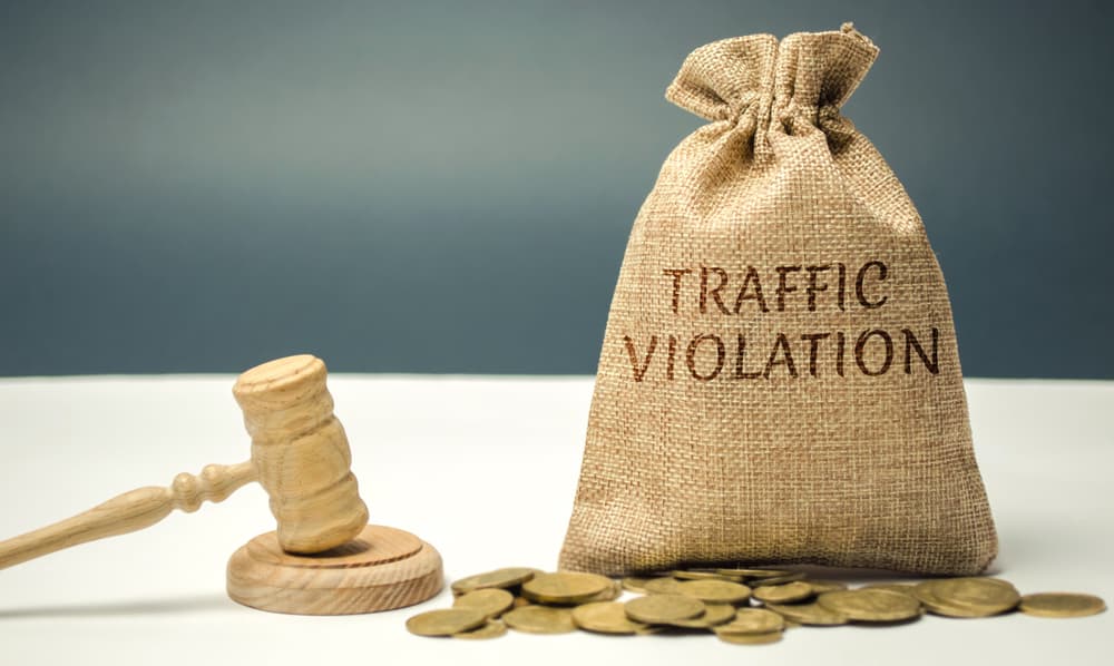 A gavel next to a sack labeled "Traffic Violation" with coins scattered around it.