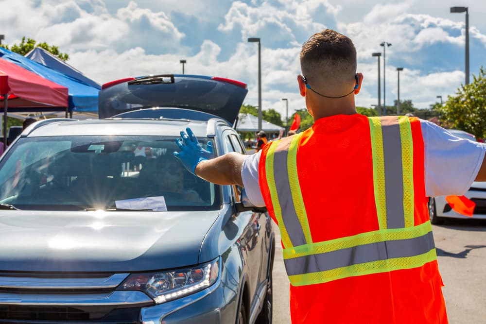 A traffic officer wearing a high-visibility vest directs a vehicle at a checkpoint outdoors.