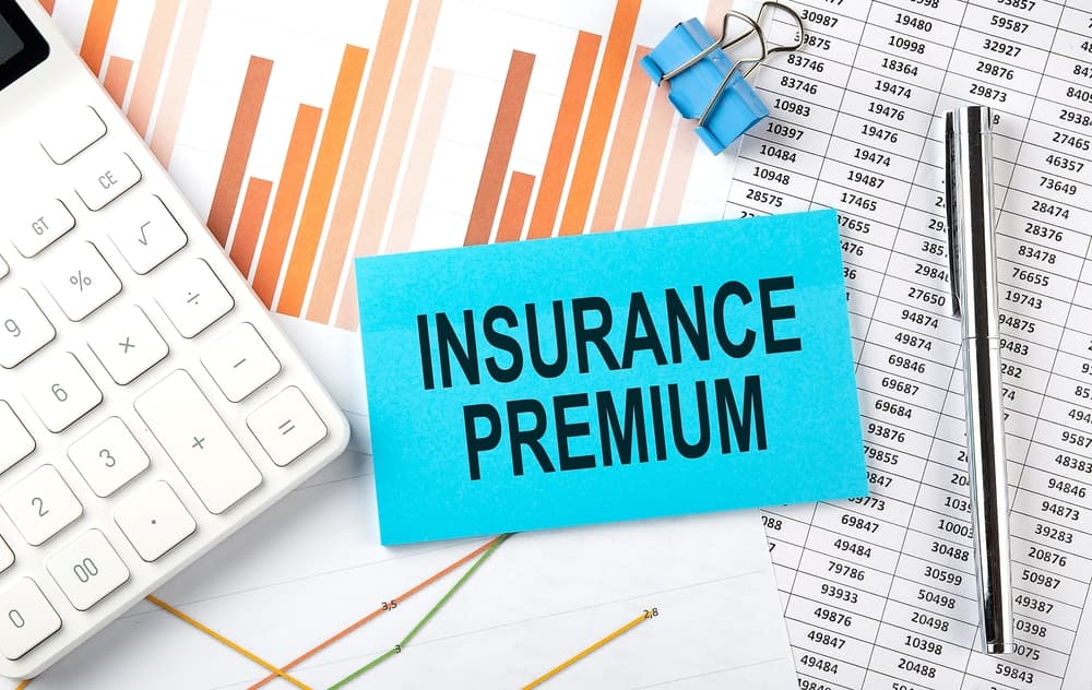 A close-up of a sticker with the text "INSURANCE PREMIUM" prominently displayed, placed on a background featuring a diagram with charts and data lines. The diagram's design includes colorful bars and curves, symbolizing financial or analytical information, adding a professional and business-oriented context.