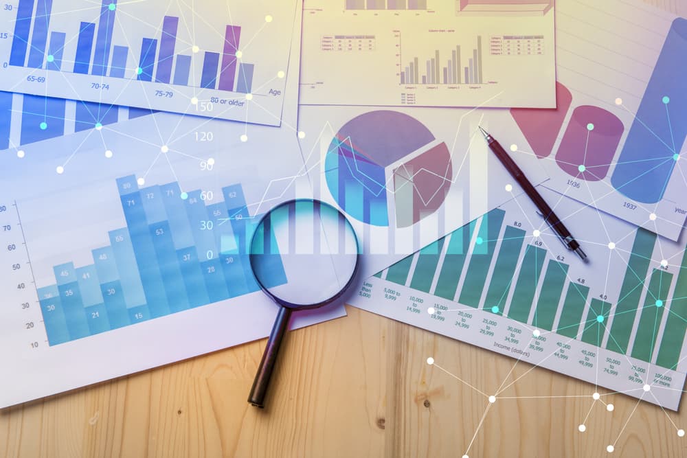 A magnifying glass placed over documents with analytics data, lying on a table, symbolizing detailed examination and analysis of business or legal information.