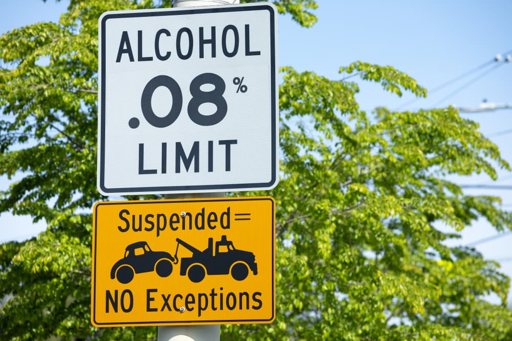 Alcohol Limit .08%" and "Suspended License = Towed Car. No Exception" road signs along a roadway