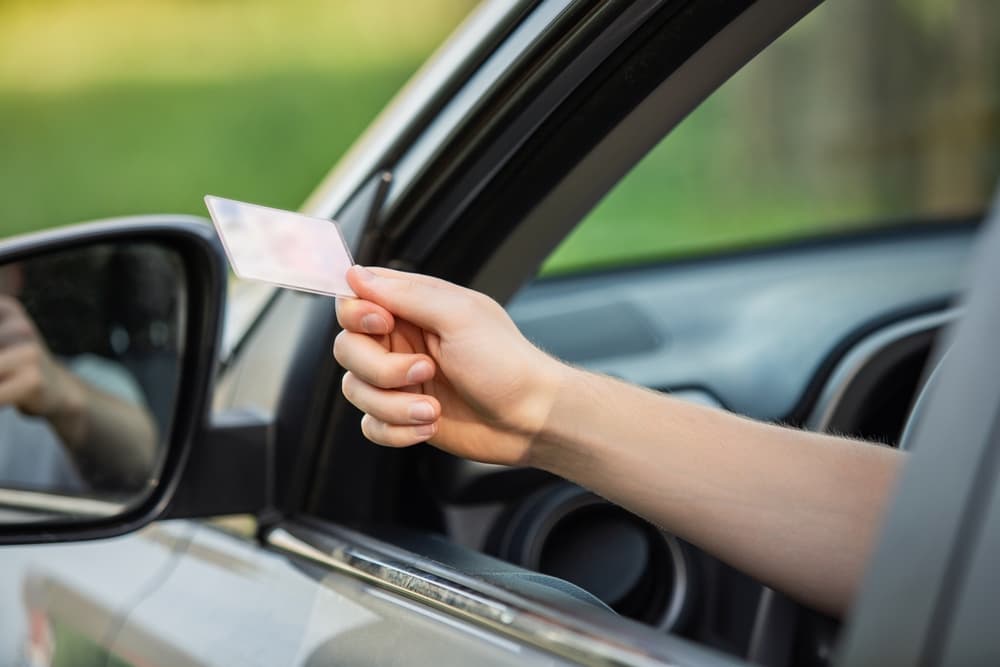 person hand out of the car window holding the driver license as shows it to the police officer at traffic stop